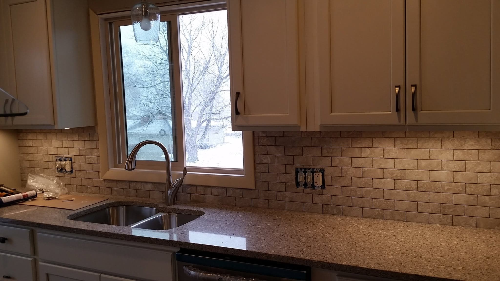 Completed kitchen with brown cabinets, brick backsplash, granite countertop, and window over sink