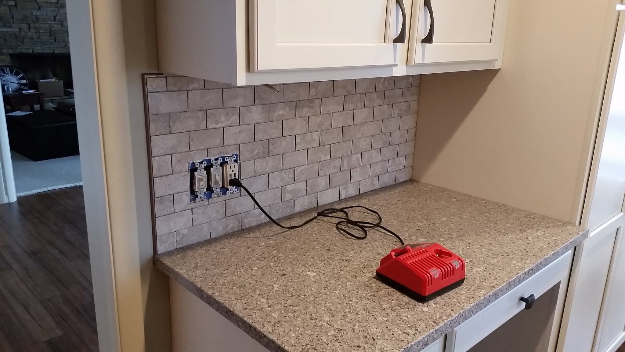 Kitchen countertop installation in progress with red cordless tool on granite surface and tile backsplash
